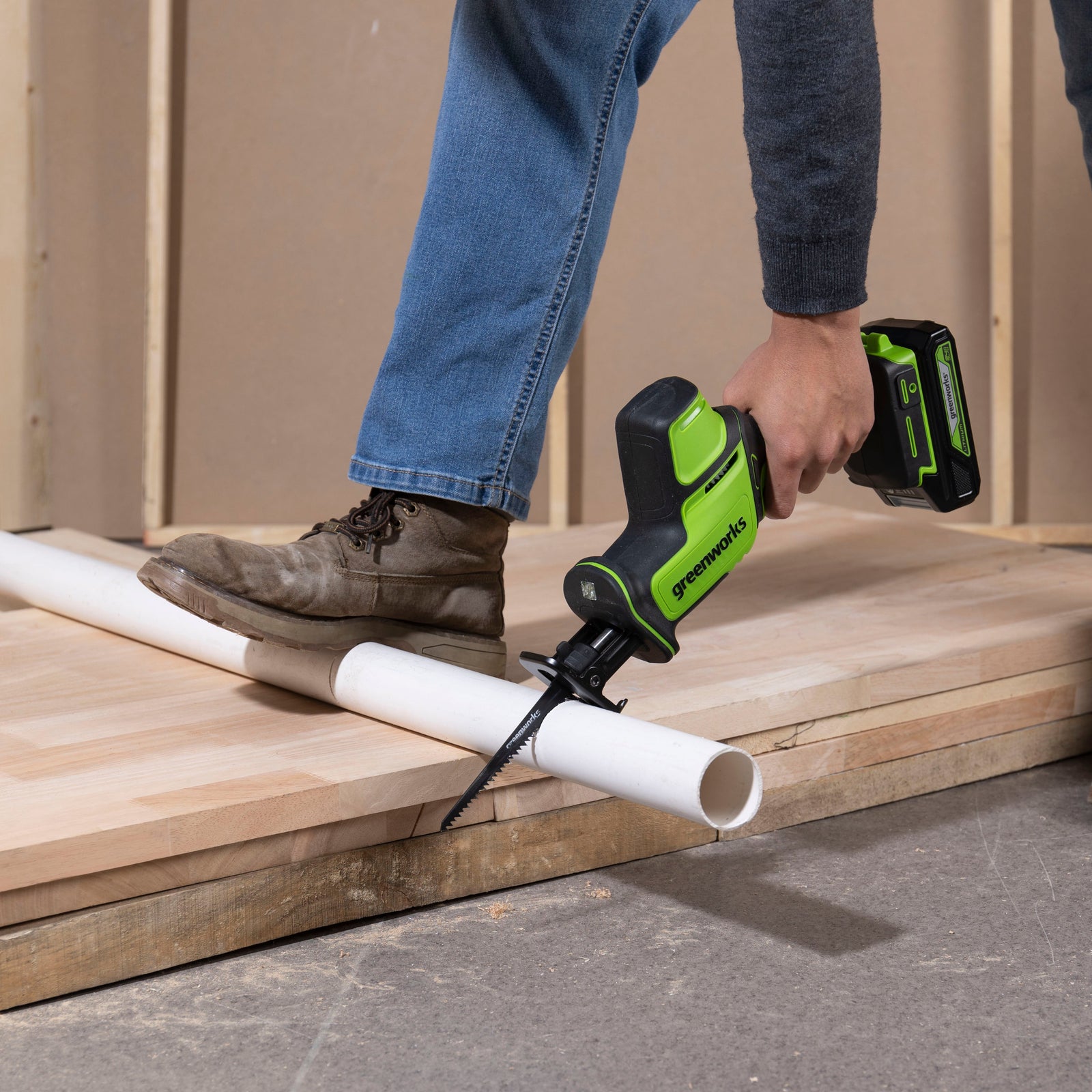 Person using a nail gun on wooden planks with a white pipe in the foreground.